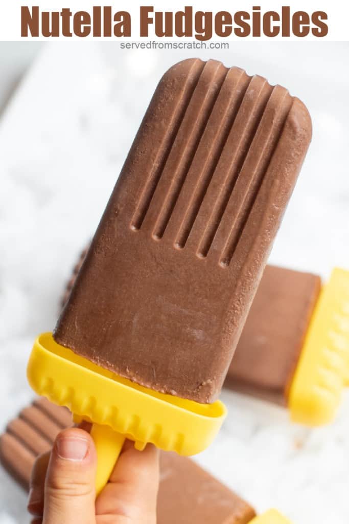 a kid's hand holding a fudgesicle with Pinterest pin text.