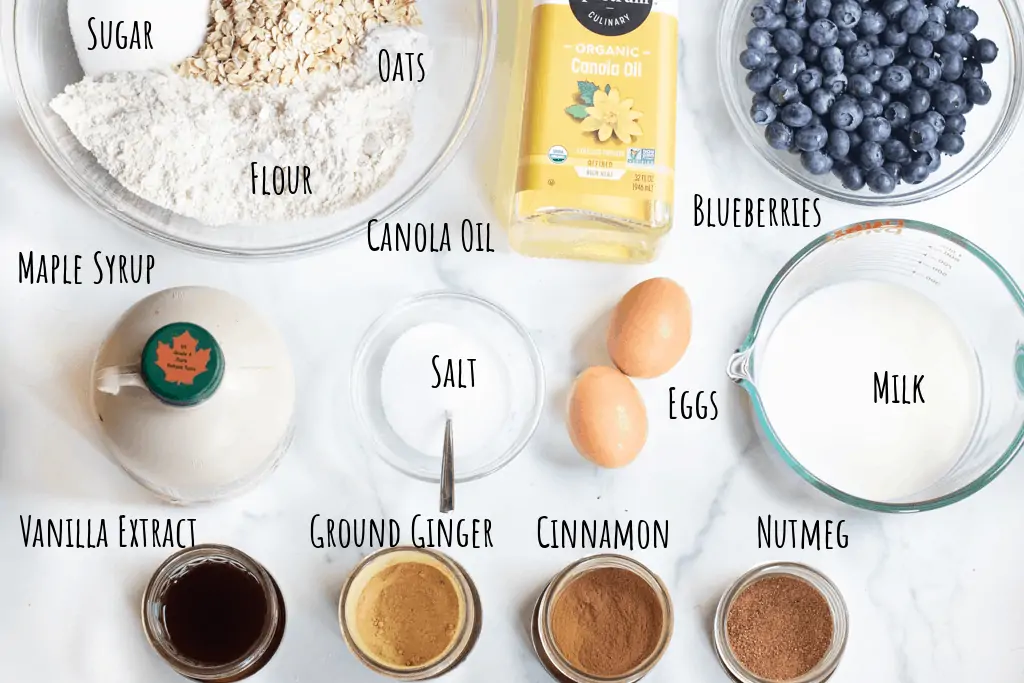 a bowl with sugar, oats, and flour, canola oil, fresh blueberries, maple syrup, eggs, salt, milk, vanilla extract, cinnamon, ground ginger, and nutmeg.