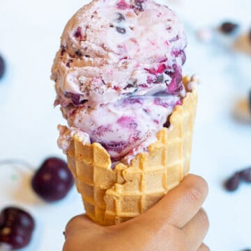 a little hand holding a waffle cone of cherry ice cream.