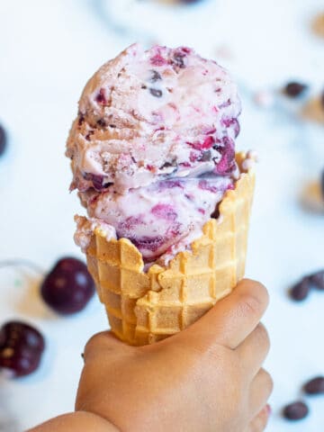 a little hand holding a waffle cone of cherry ice cream.