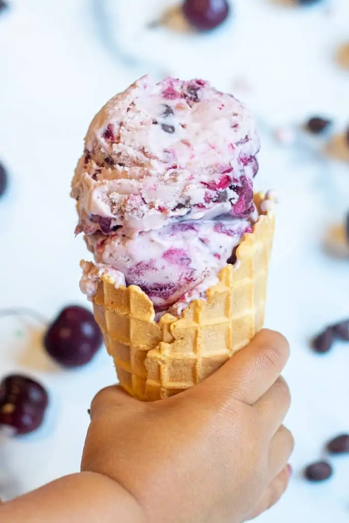 a little hand holding a waffle cone of cherry ice cream.