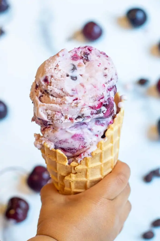 a kid hand holding a waffle cone with cherry ice cream.