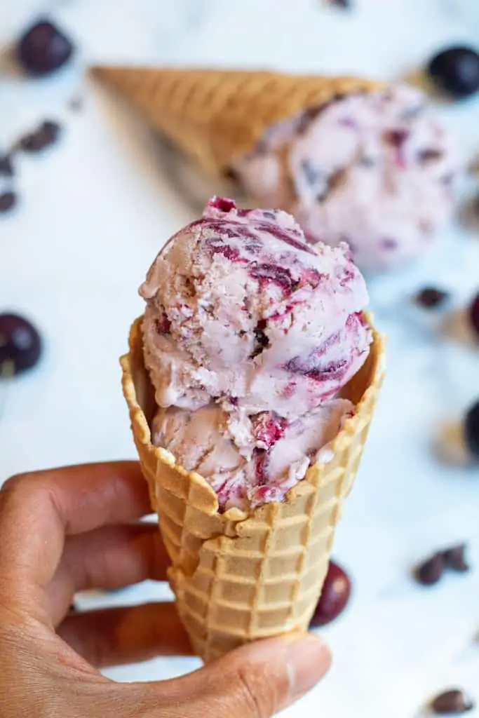 a hand holding a waffle cone with cherry ice cream.