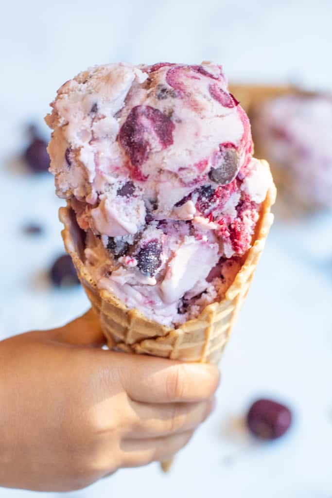 a little hand holding a waffle cone of cherry ice cream.