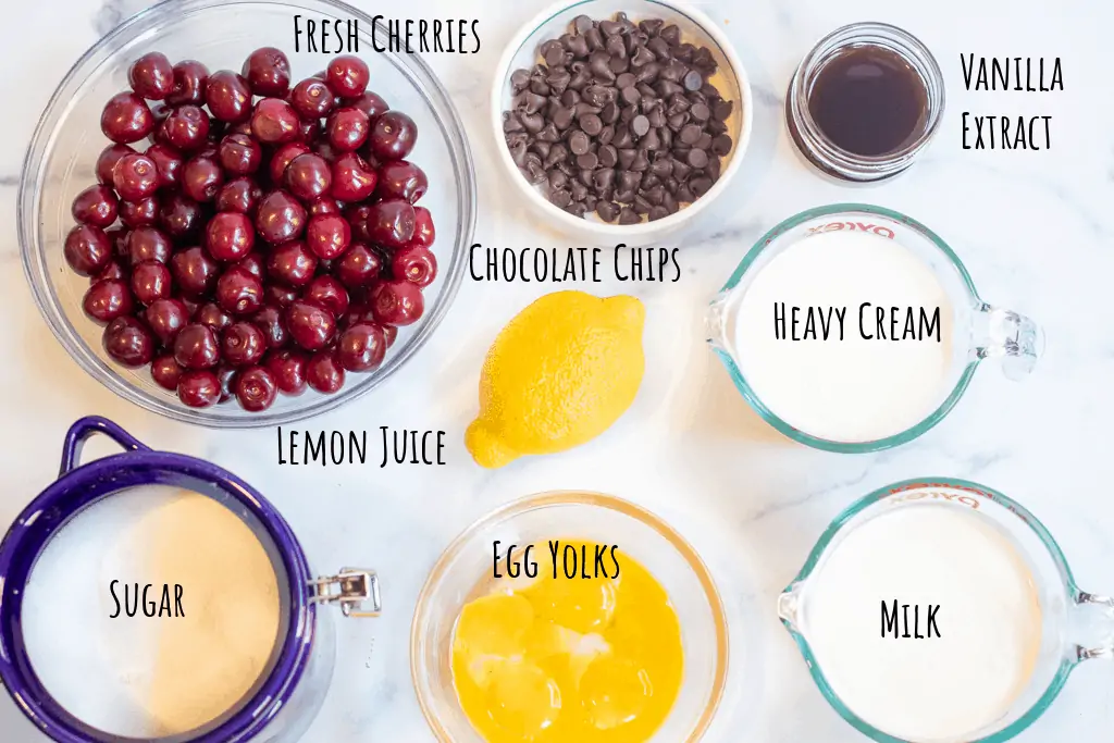 cherries, chocolate, vanilla, milk, cream, lemon, sugar, egg yolks on a counter.