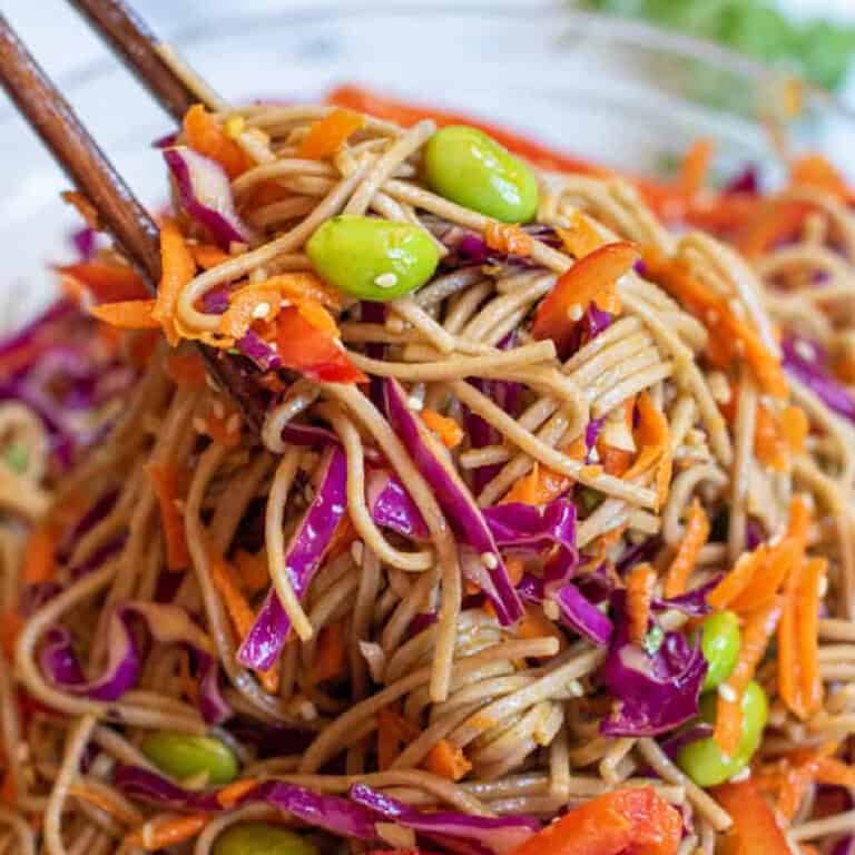 chopsticks holding up some noodles with edamame, carrots, cabbage, and red pepper.