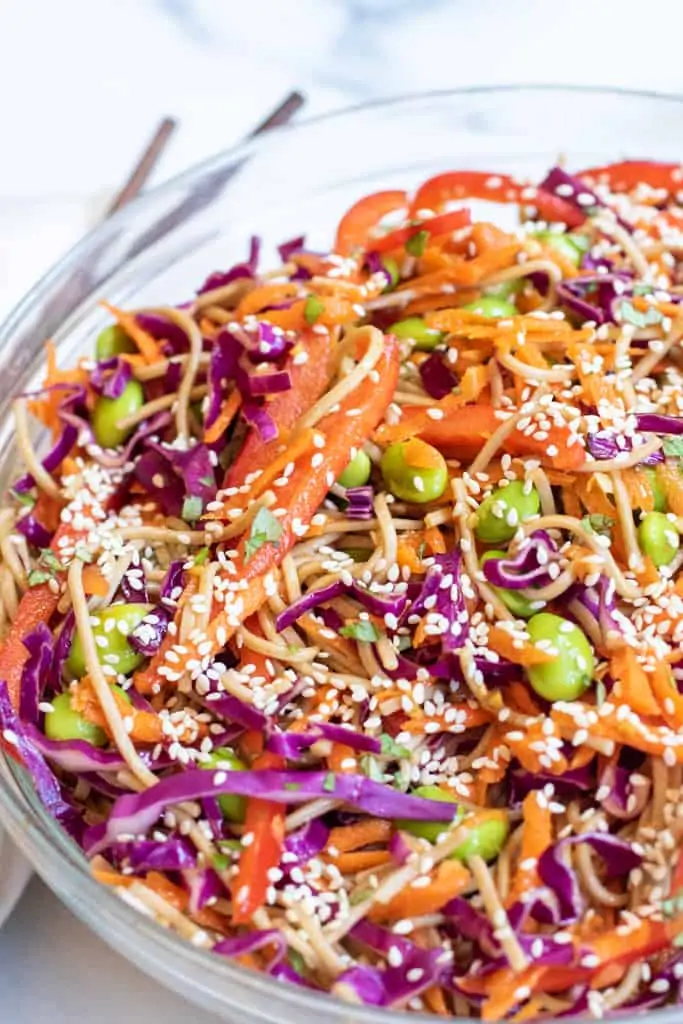 a bowl of soba noodles with cabbage, carrots, edamame, and sesame seeds.