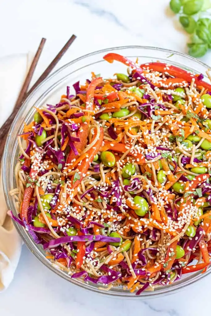 a bowl of soba noodles with cabbage, carrots, edamame, and sesame seeds.