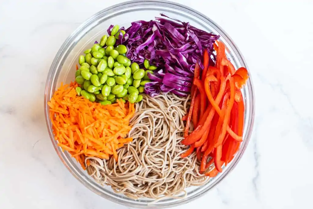 soba noodles, carrots, sliced red pepper, cabbage, and edamame in a bowl.