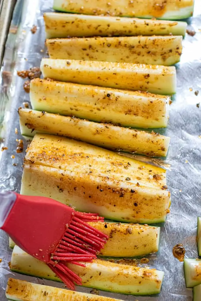 a brush putting oil and herbs on zucchini spears.