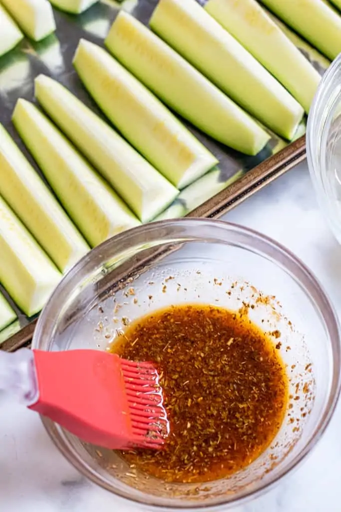 a bowl of oil and herbs next to zucchini spears.