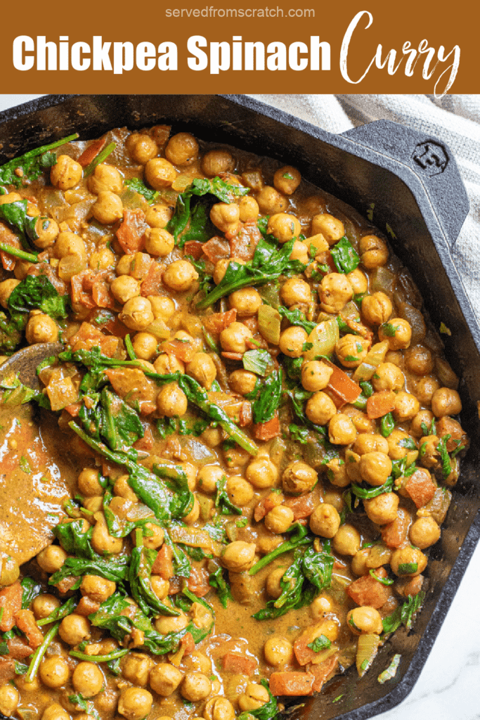 a cast iron of chickpea curry with spinach with a wooden spoon with Pinterest pin text.