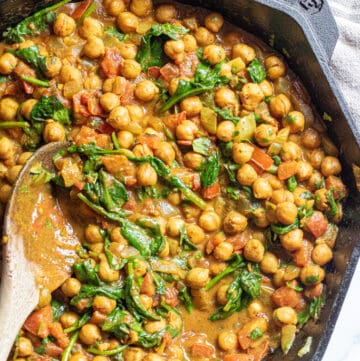 a cast iron of chickpea curry with spinach with a wooden spoon.