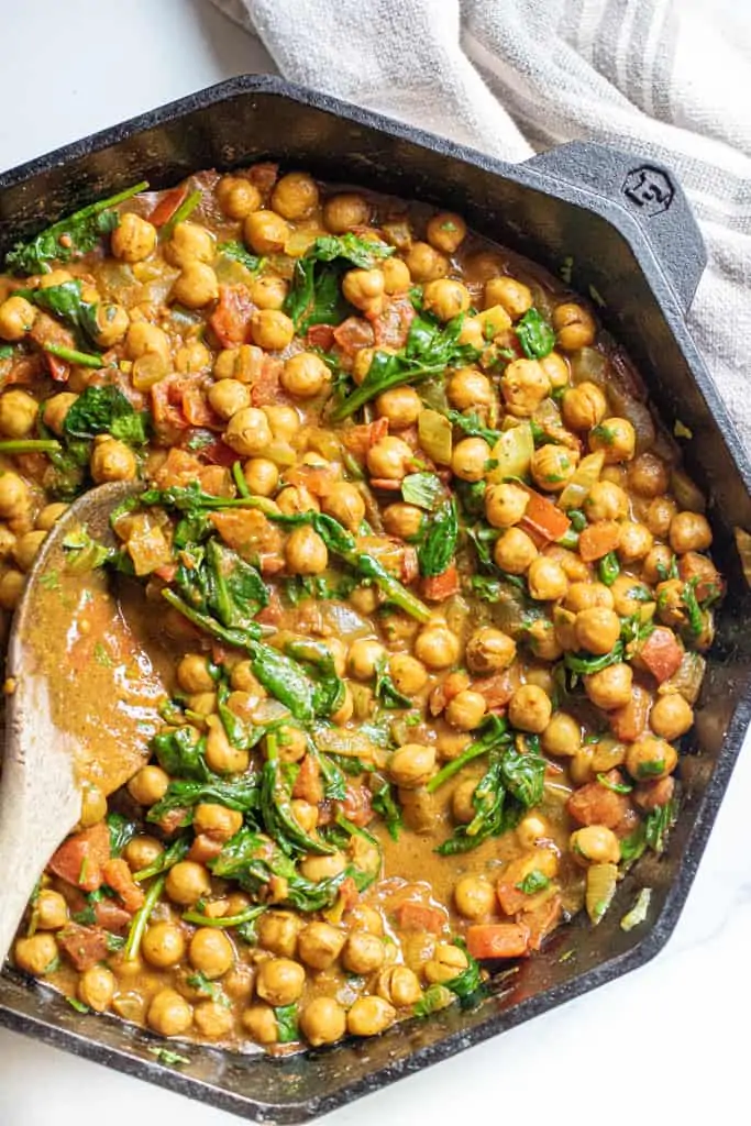 a cast iron of chickpea curry with spinach with a wooden spoon.