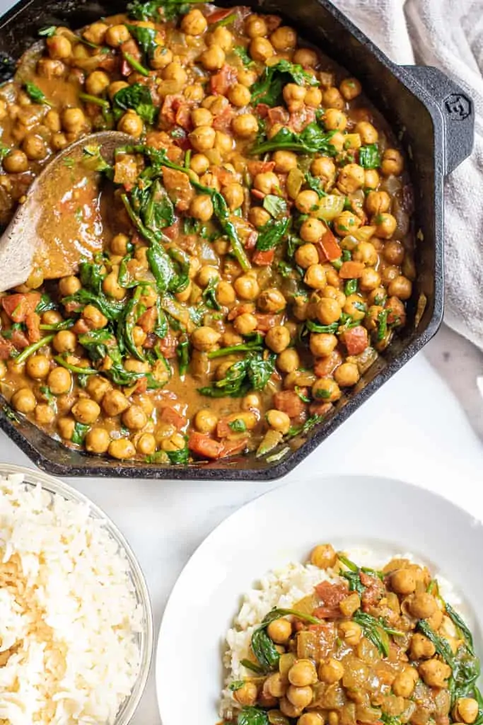 an overhead of cast iron with chickpea curry next to plate of curry over rice and a bowl of rice.