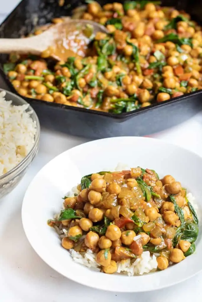 a bowl of chickpea curry over rice next to a bowl of rice in front of a cast iron.