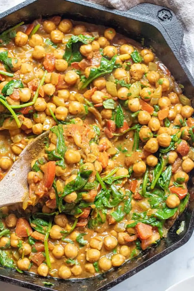 a cast iron of chickpea curry with spinach with a wooden spoon.