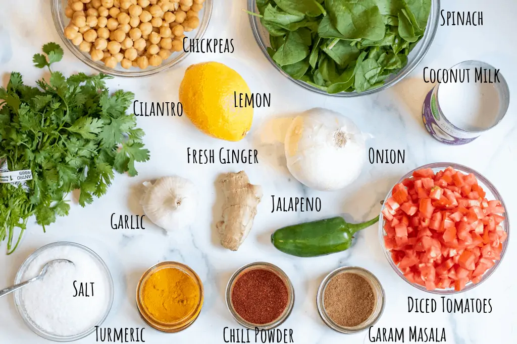 cilantro, chickpeas, spinach, tomatoes, lemon, onion, coconut milk, ginger, garlic, spices on counter.