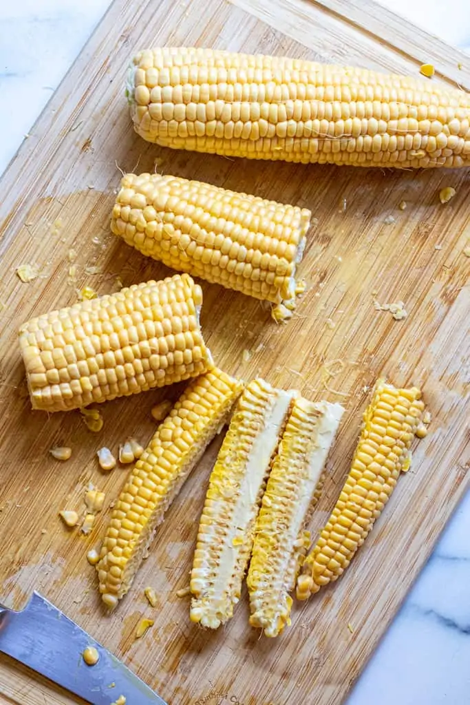 a whole ear of corn, two halves, and then one half quartered on a cutting board.