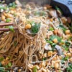 cast iron of noodles with spinach, mushrooms, topped with peanuts and scallions chopsticks holding up noodles.