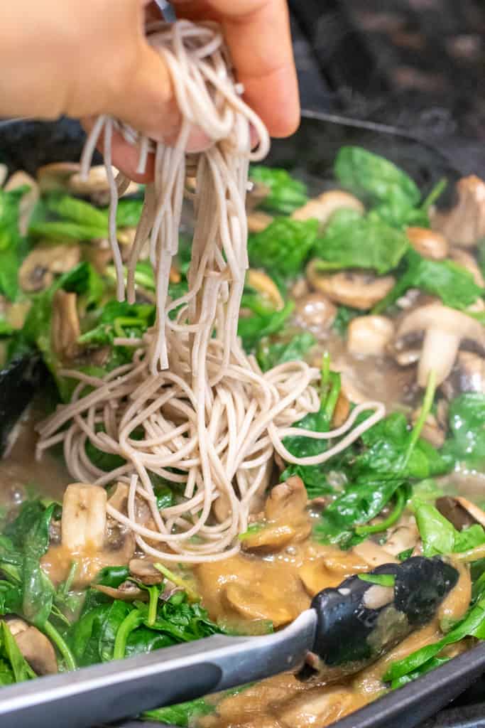 noodles being added to a pan with cooked spinach, mushrooms, and miso sauce.