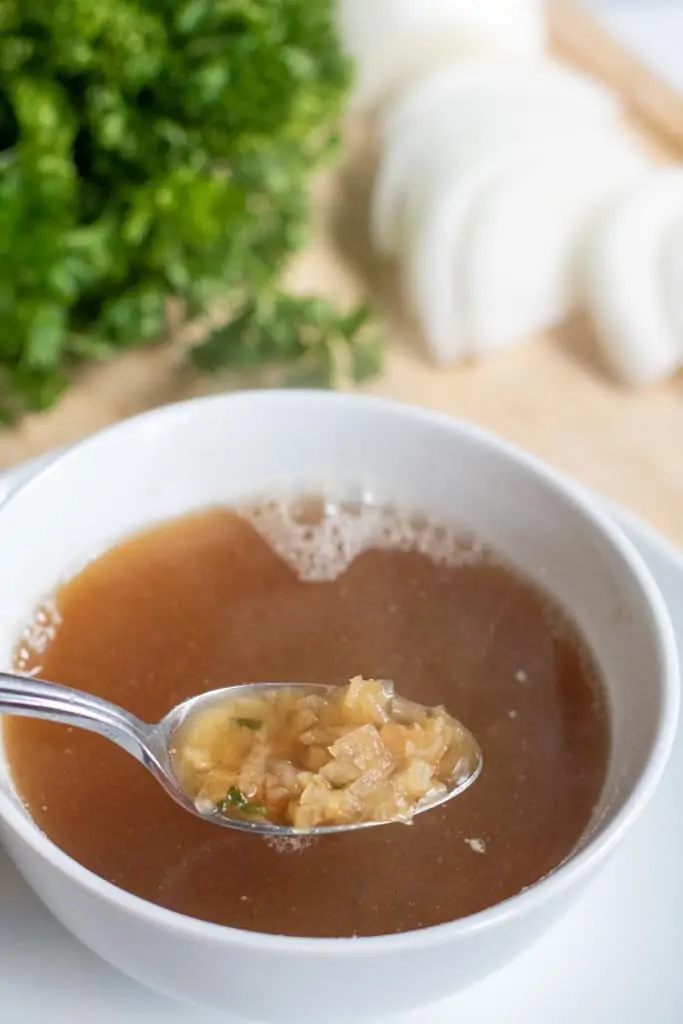 a small bowl of onion soup with a spoon scooping out some onions.