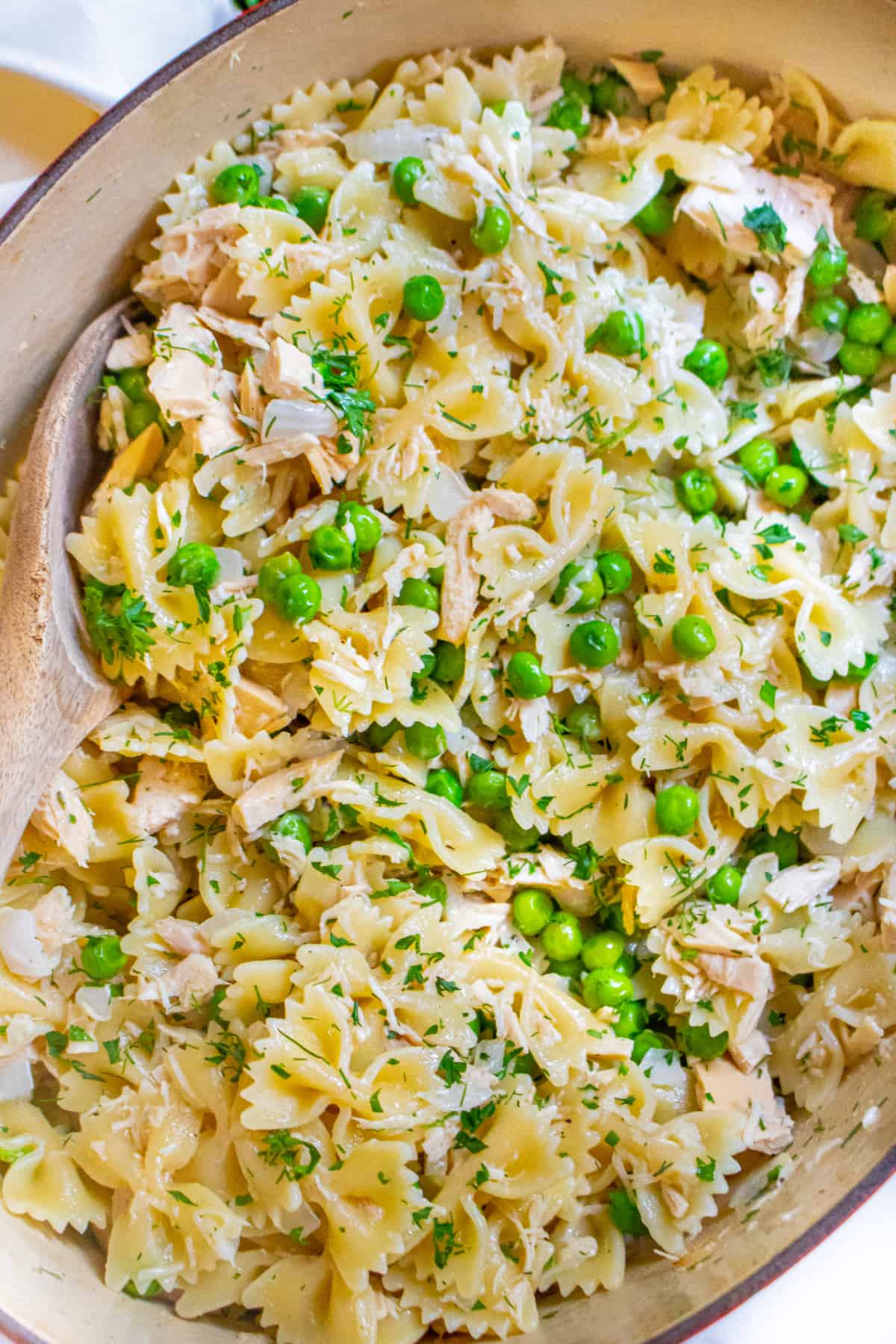 a pot of pasta, peas, and tuna with a wooden spoon.