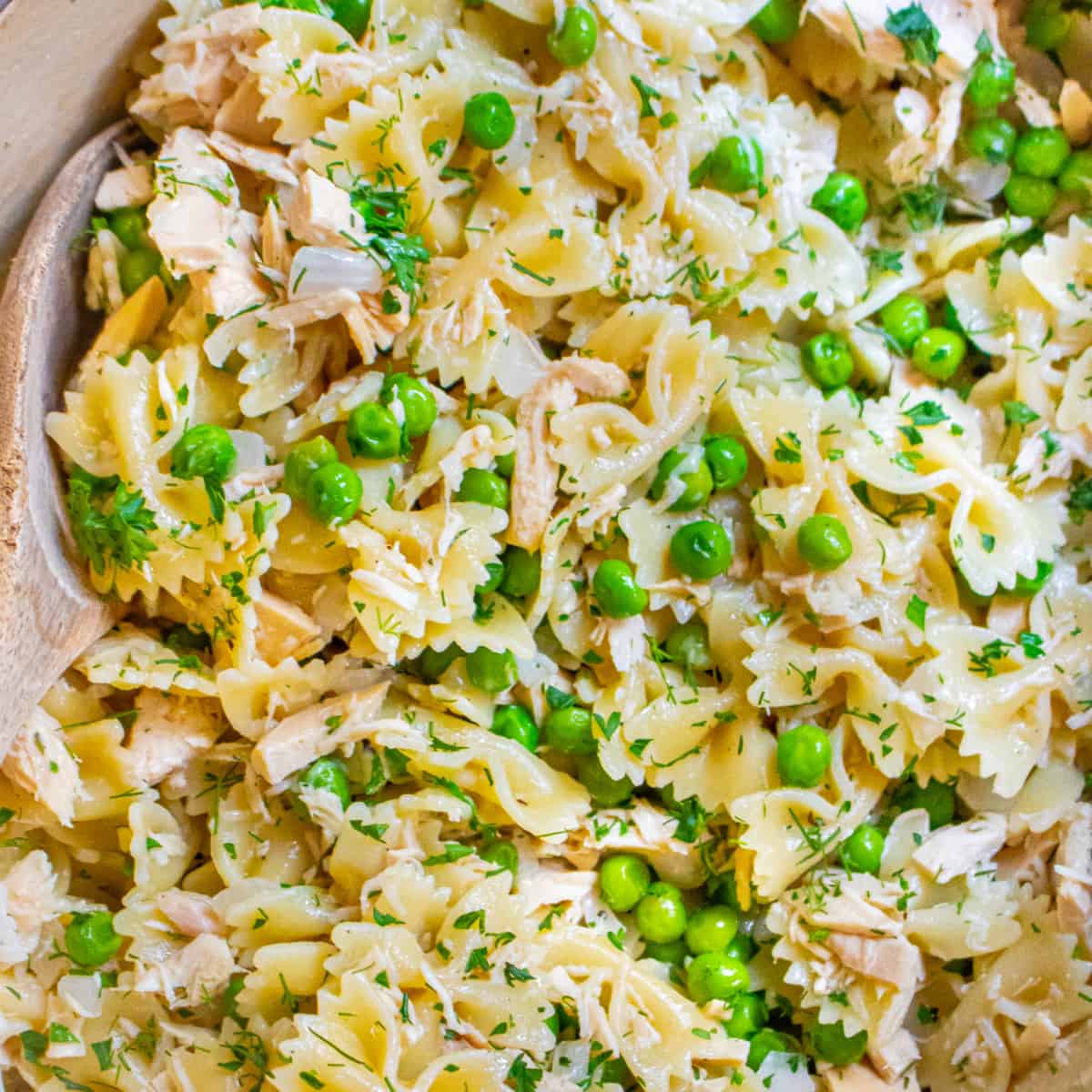 a pot of pasta, peas, and tuna with a wooden spoon.