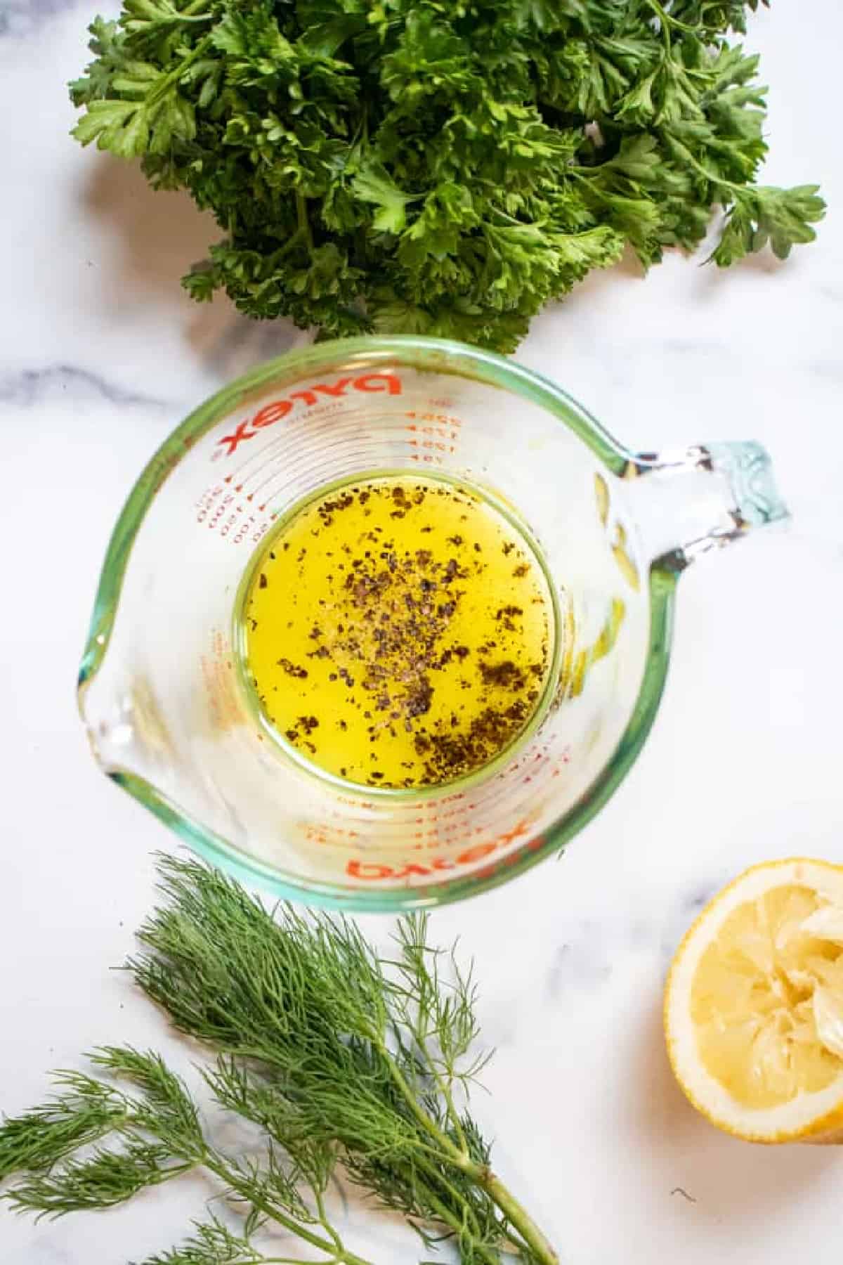 Pyrex with vinaigrette and herbs surrounding it.