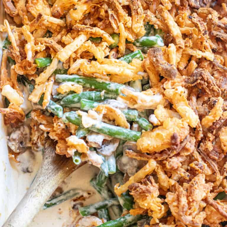 an overhead of a green bean casserole with fresh green beans and lots of french's fried onions with a spoon in it.