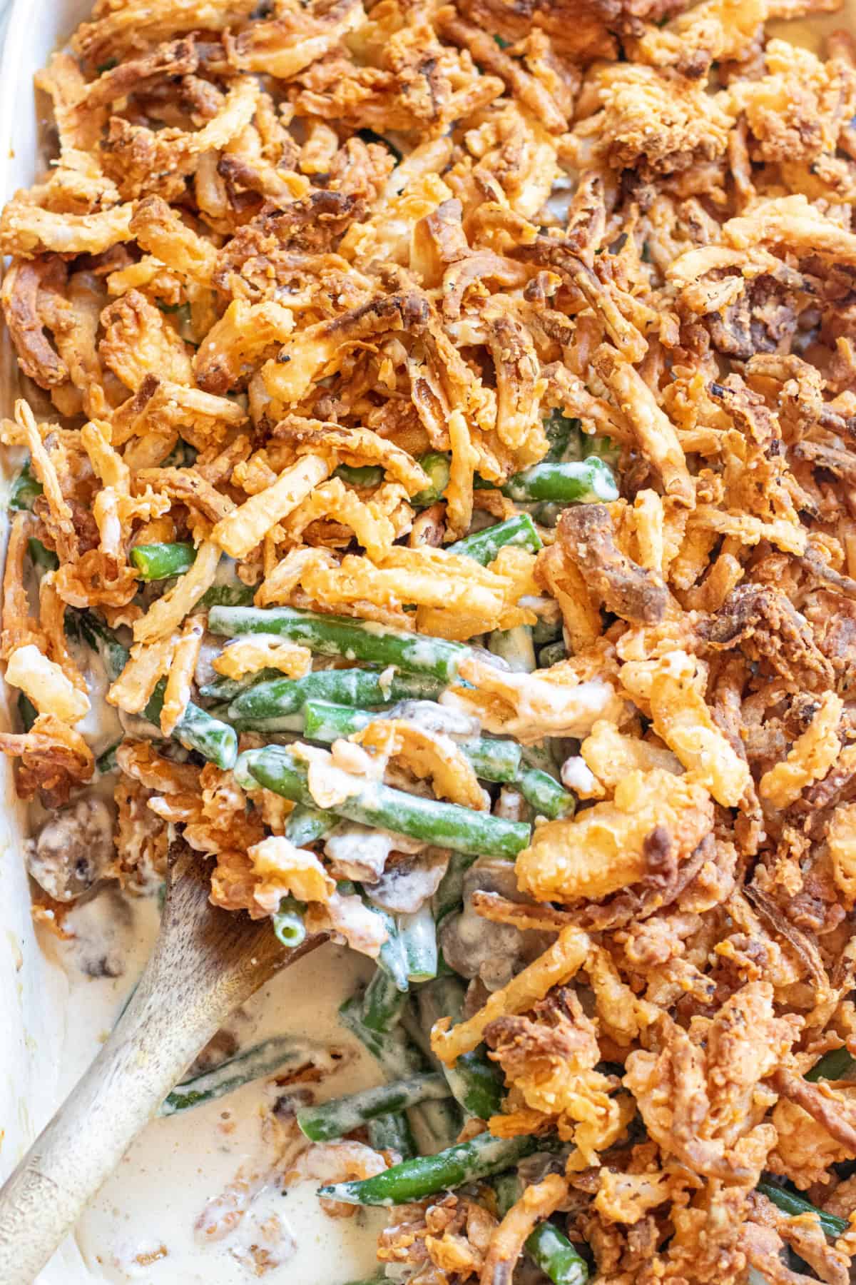 an overhead of a green bean casserole with fresh green beans and lots of french's fried onions with a spoon in it.