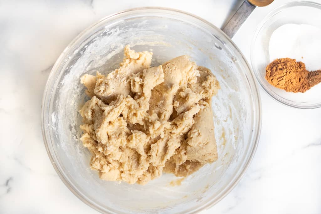 a bowl of mixed dough with small bowl of cinnamon and sugar on the side.