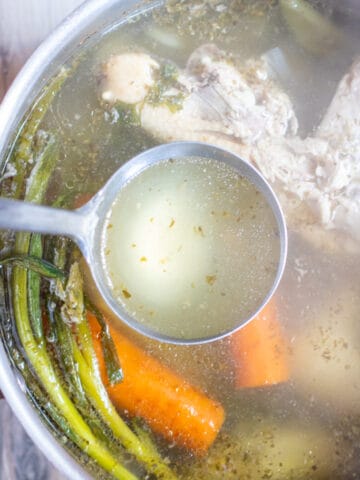 a spoon ladle with some stock from a pot with chicken and veggies.