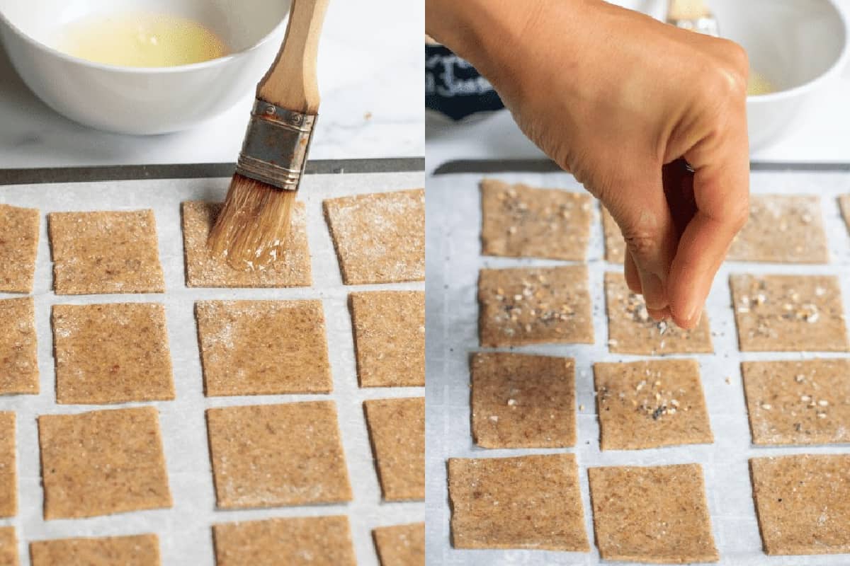 egg washing cracker dough and then a hand sprinkling seasoning on unbaked crackers.