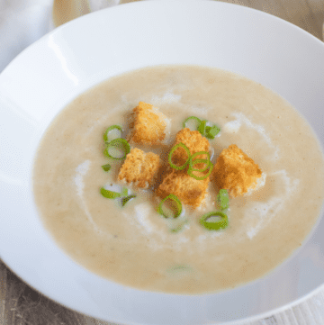 a bowl of creamy soup with croutons and onions.