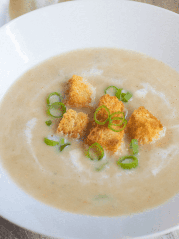 a bowl of creamy soup with croutons and onions.