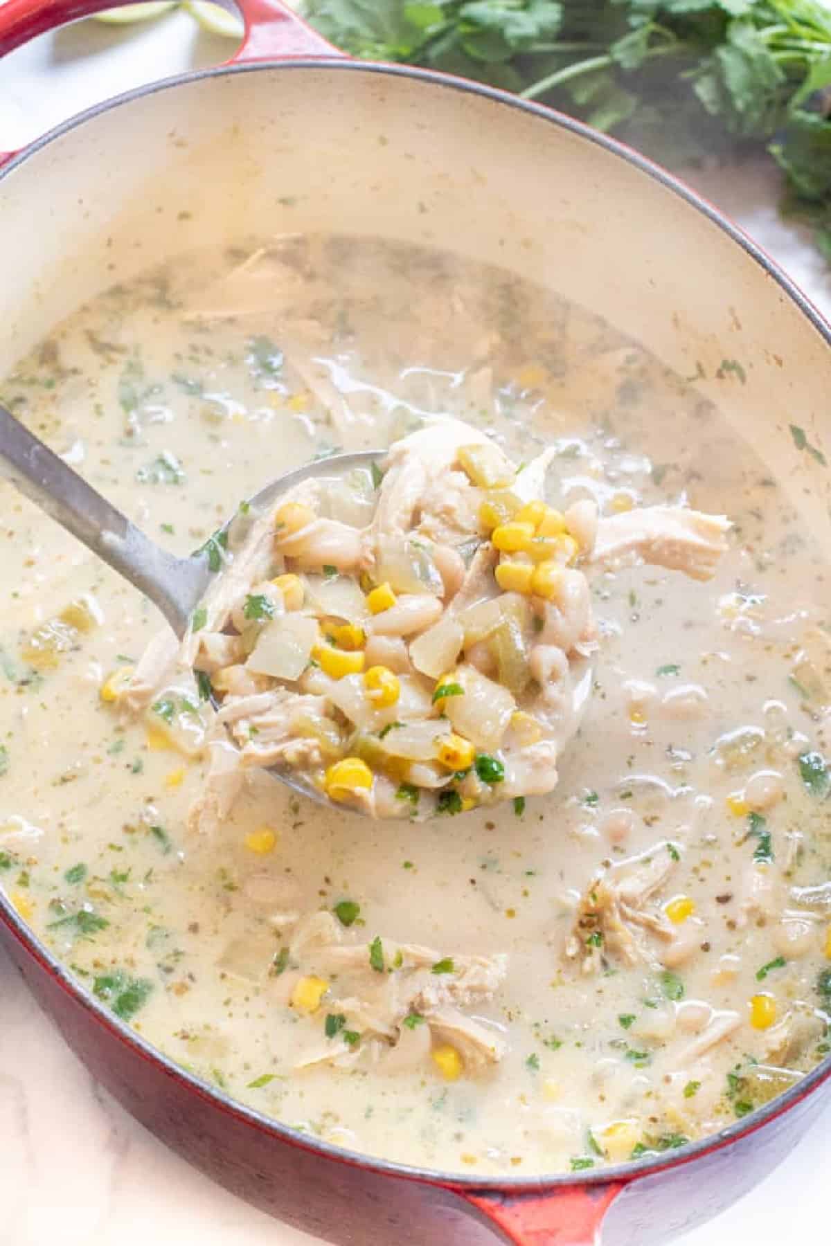 a dutch oven with white chili and a ladle with a scoop.