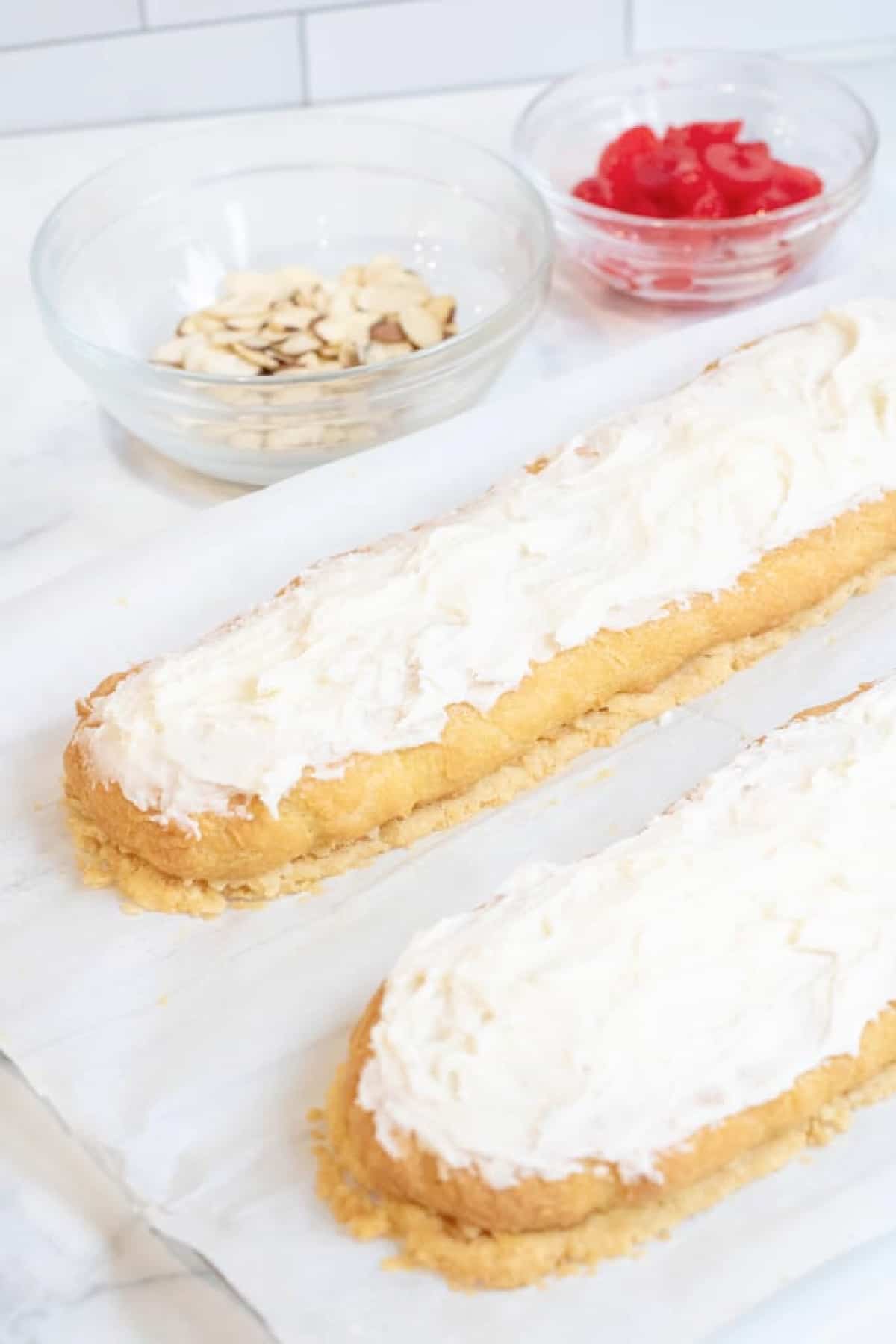 two frosted puff pastries with a bowl of sliced almonds and a bowl of cherries.