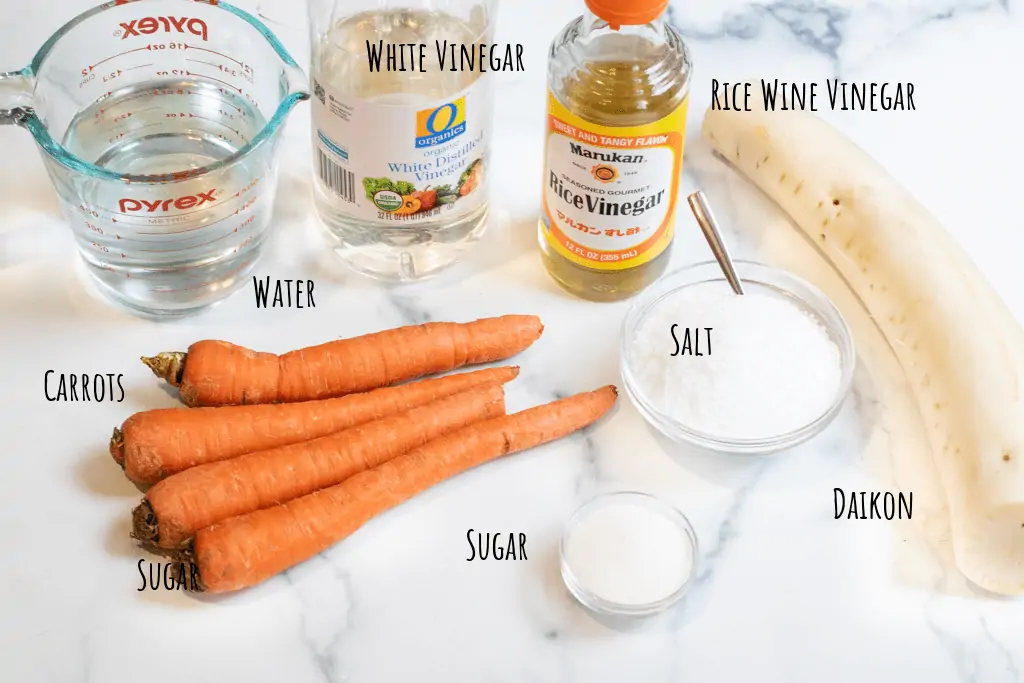 carrots, daikon, vinegar, rice vinegar, salt, sugar, water on a counter.