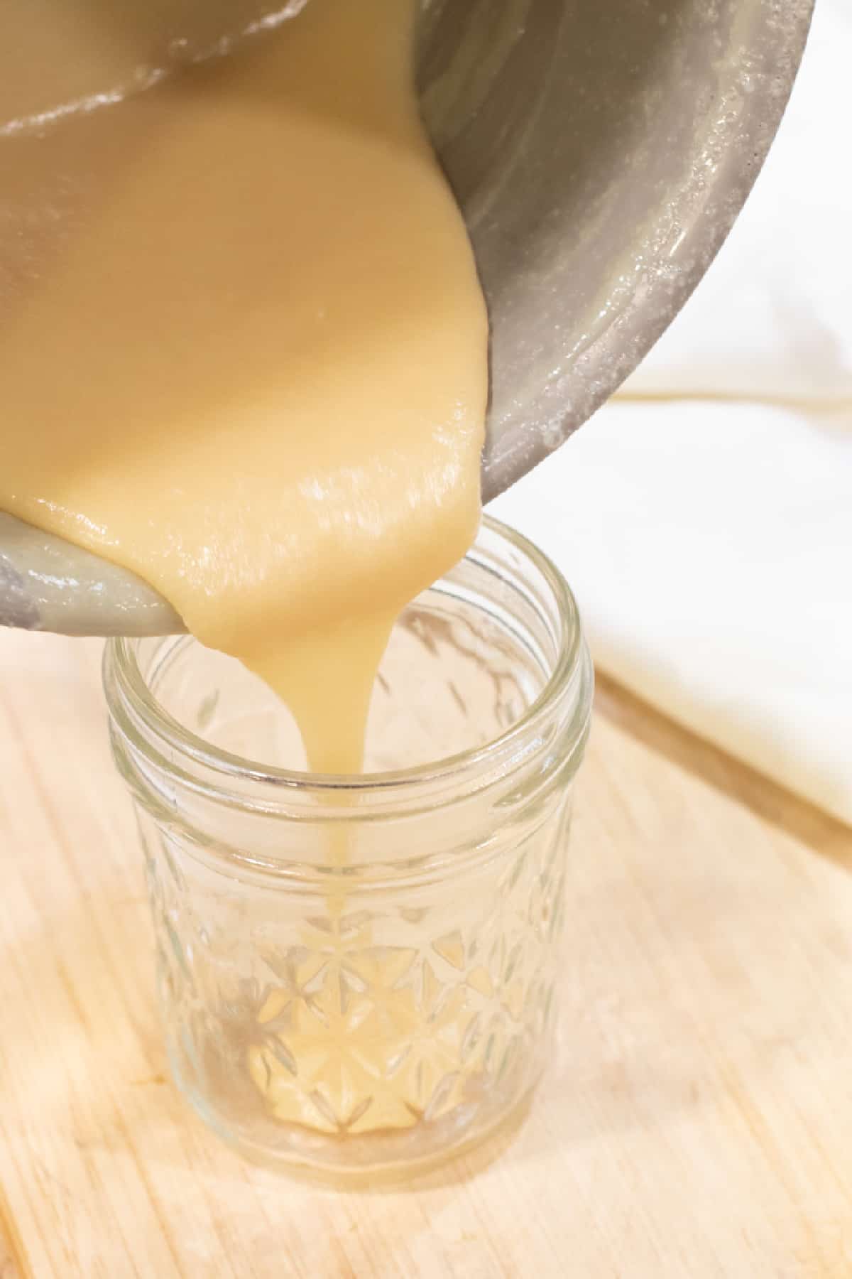 condensed milk being poured from a pan to a mason jar.