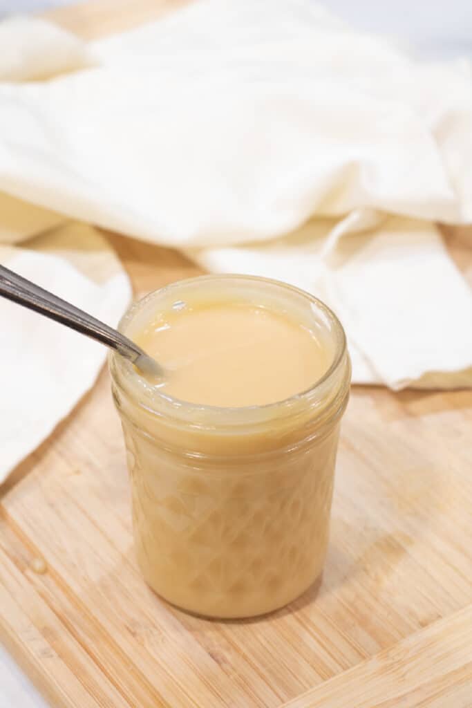 an open jar with a spoon of condensed milk.