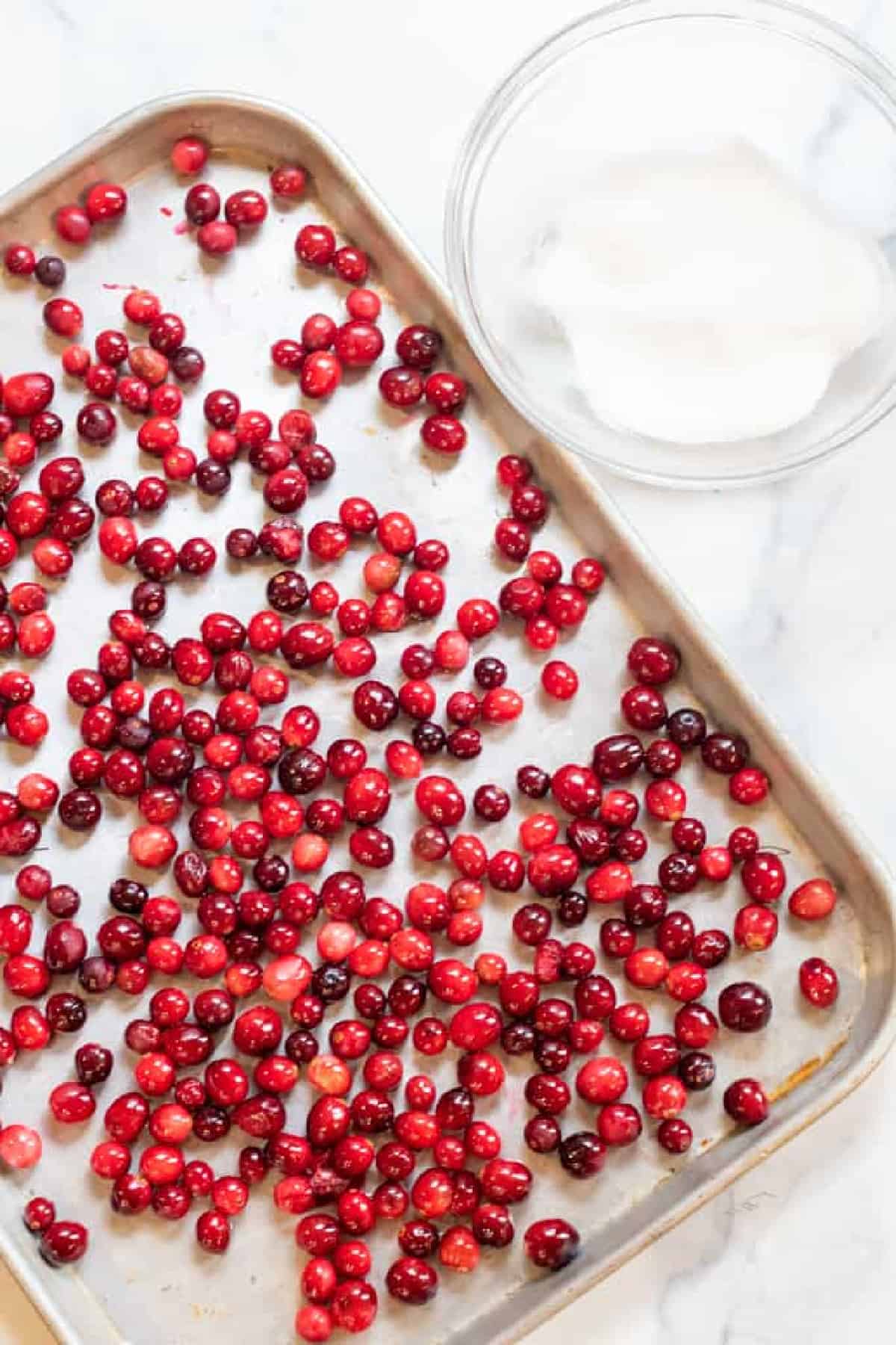 a baking sheet with fresh cranberries next to a bowl of sugar.