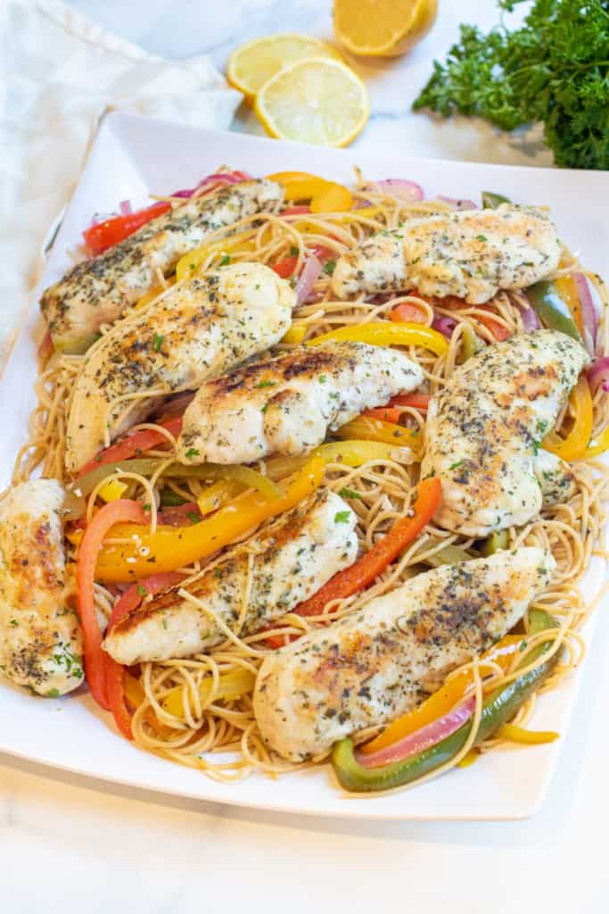 a large platter of pasta with cooked peppers and chicken.