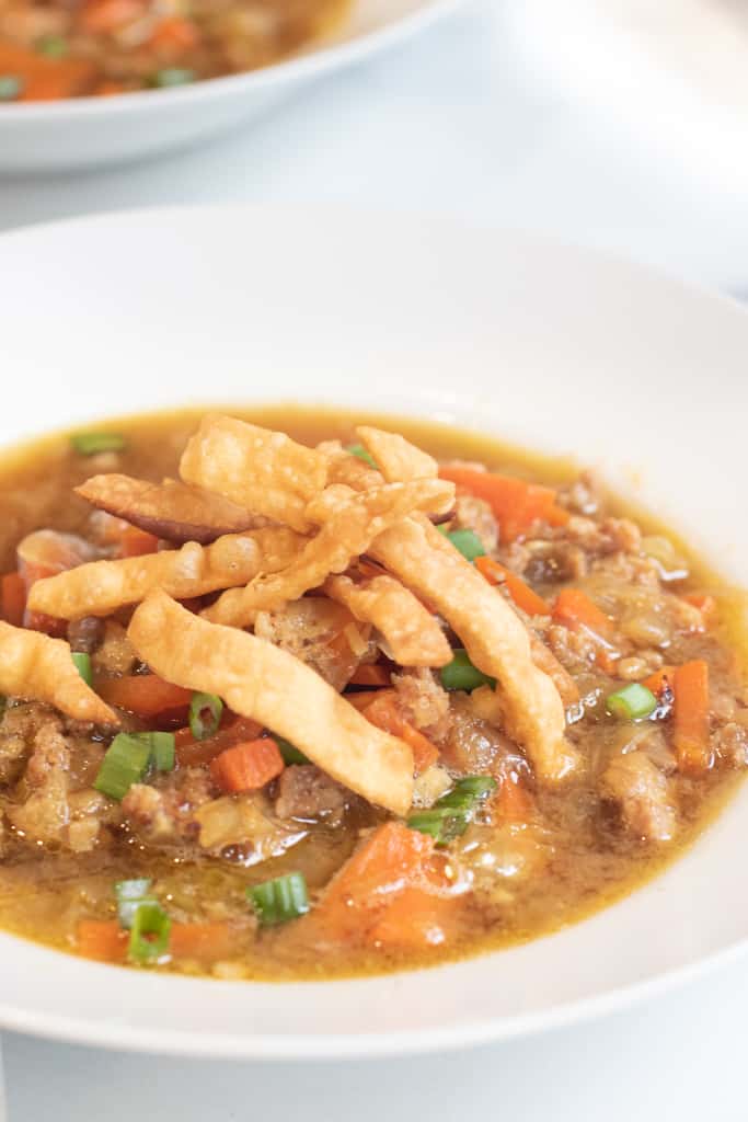 a bowl of soup with cabbage and carrots and pork topped with crispy strips.