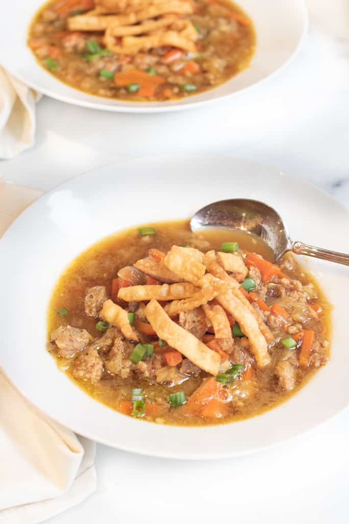 a bowl of soup with cabbage and carrots and pork topped with crispy strips and a spoon in it.