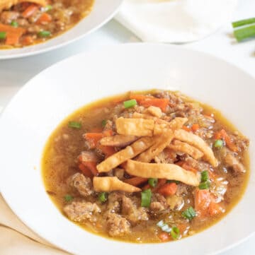 a bowl of soup with cabbage and carrots and pork topped with crispy strips.