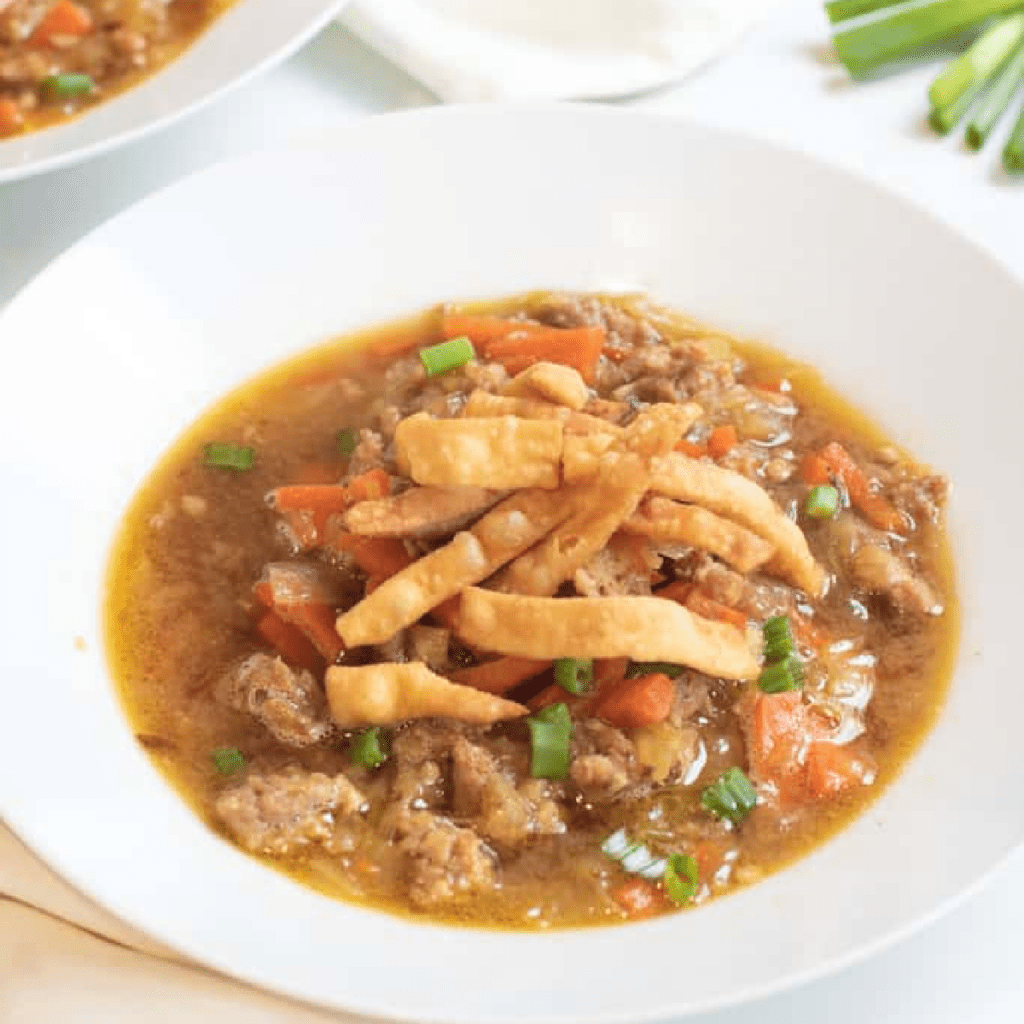 a bowl of soup with cabbage and carrots and pork topped with crispy strips.