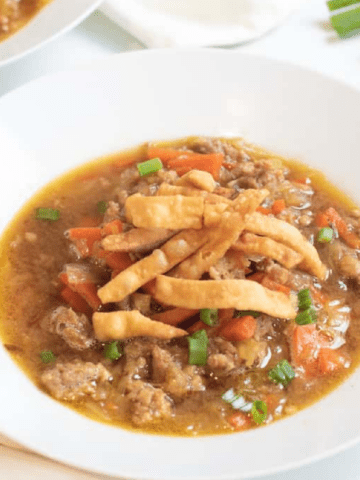 a bowl of soup with cabbage and carrots and pork topped with crispy strips.