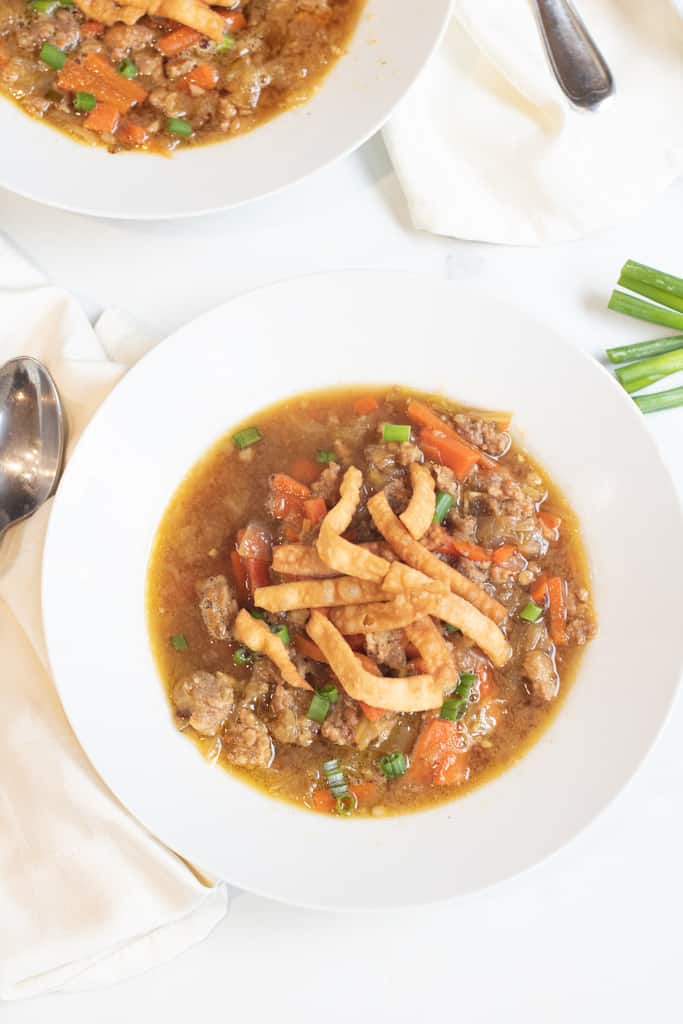 a bowl of soup with cabbage and carrots and pork topped with crispy strips.