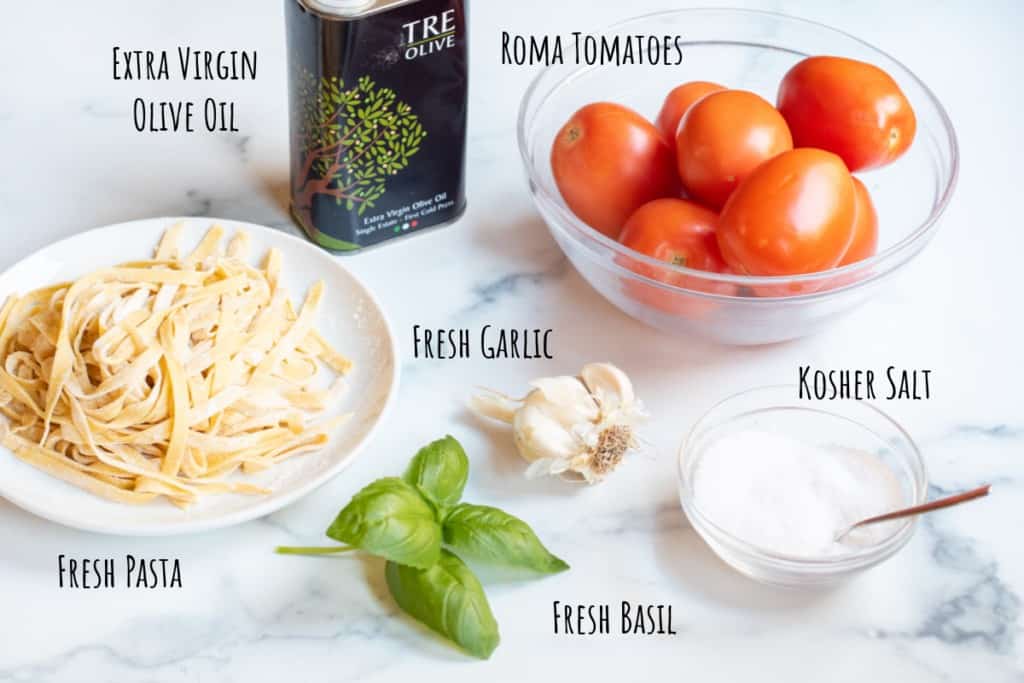 fresh pasta, olive oil, fresh basil, garlic, salt, and tomatoes on a counter.